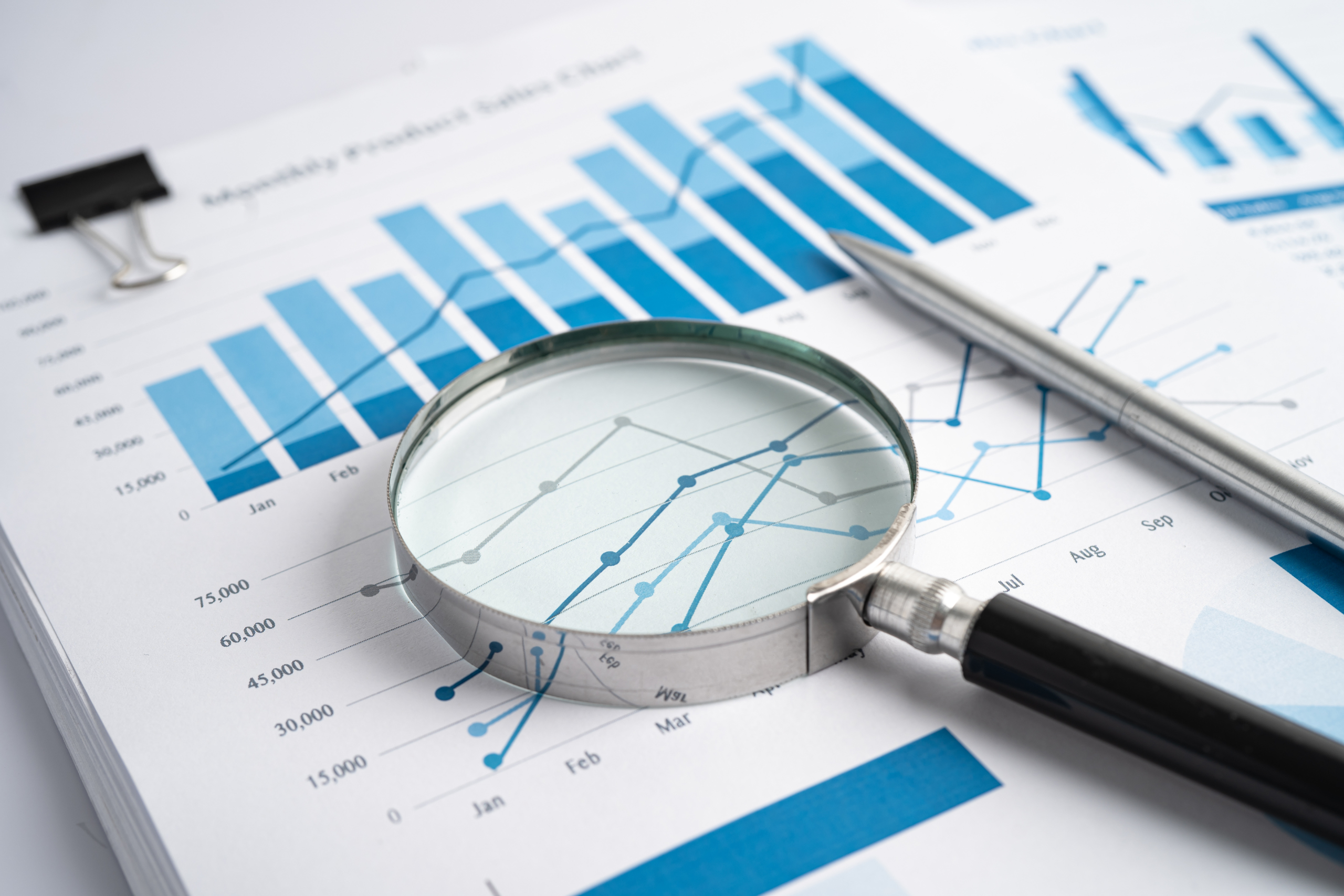 A magnifying glass resting on charts and graphs displaying financial information.