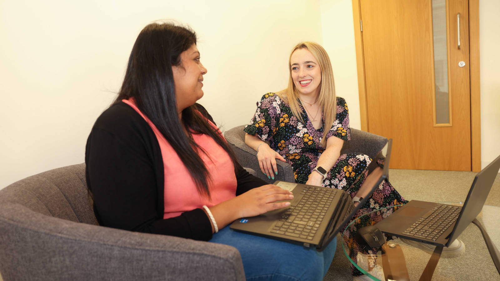 Two people sat down and having a discussion with laptops in front of them.
