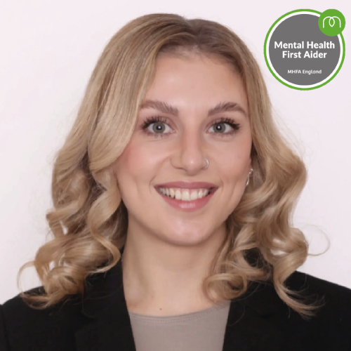 Portrait of a smiling woman with blonde hair in a blazer; MHFA England 'Mental Health First Aider' badge visible in the top-right corner.