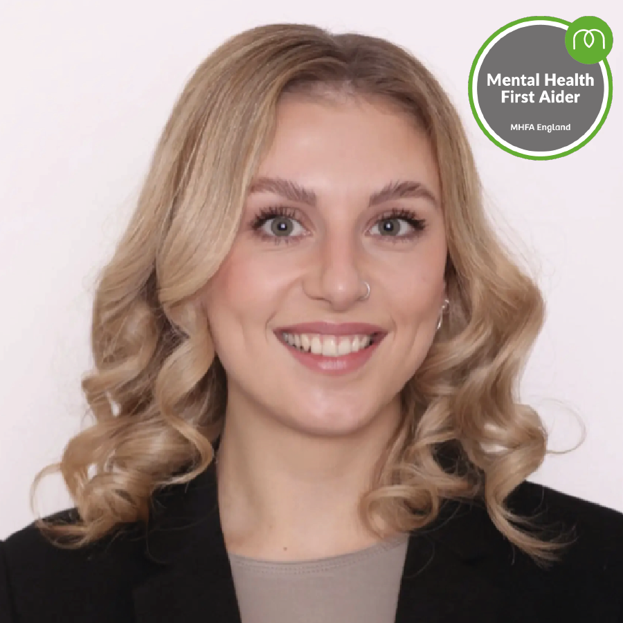 Portrait of a smiling woman with blonde hair in a blazer; MHFA England 'Mental Health First Aider' badge visible in the top-right corner.