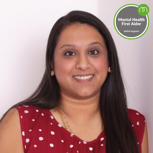 Portrait of a smiling woman in a red polka-dot top, with an MHFA England 'Mental Health First Aider' badge in the top-right.